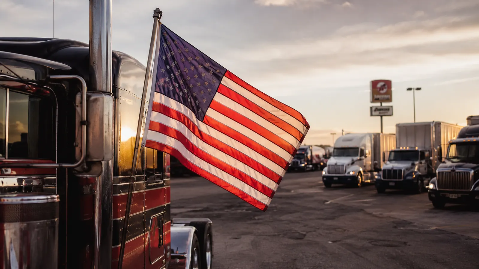 American flag flying from a semi truck at a busy truck stop at dusk