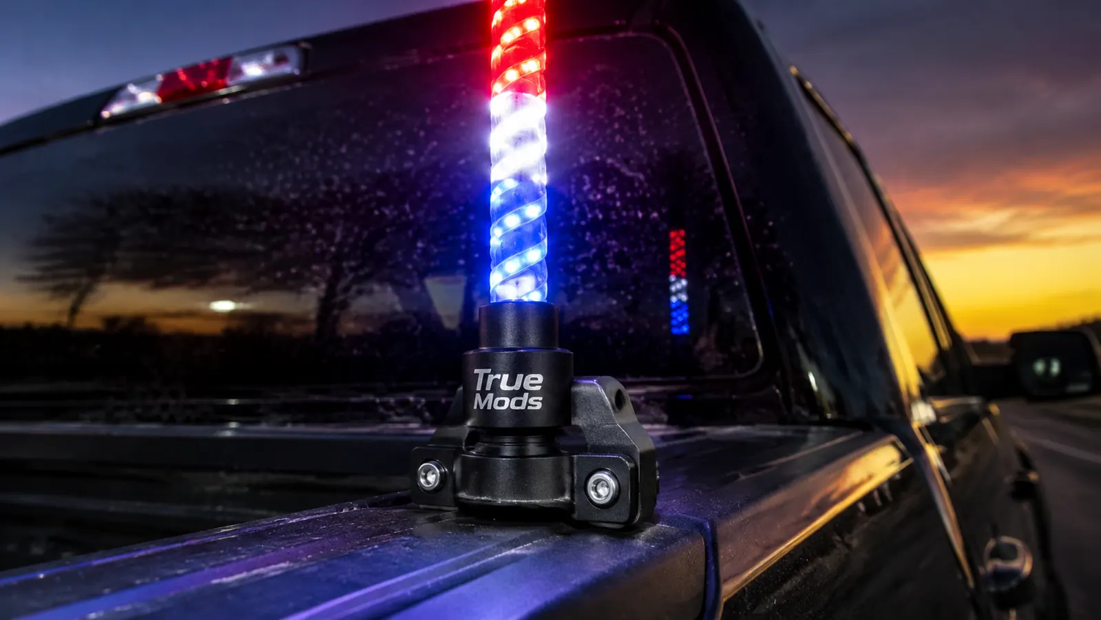 Close-up of True Mods LED whip light base mount with waterproof connectors, mounted on truck cab roof rail