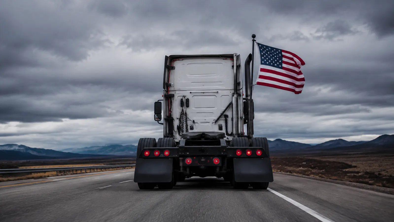 UniExtra hitch mount installed in the rear receiver of a semi truck, black steel mount holding a flagpole with American flag flying at highway speed, overcast sky